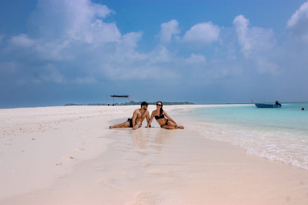 Couple having a beach picnic on the sandbank near Fodhdhoo, surrounded by turquoise water.