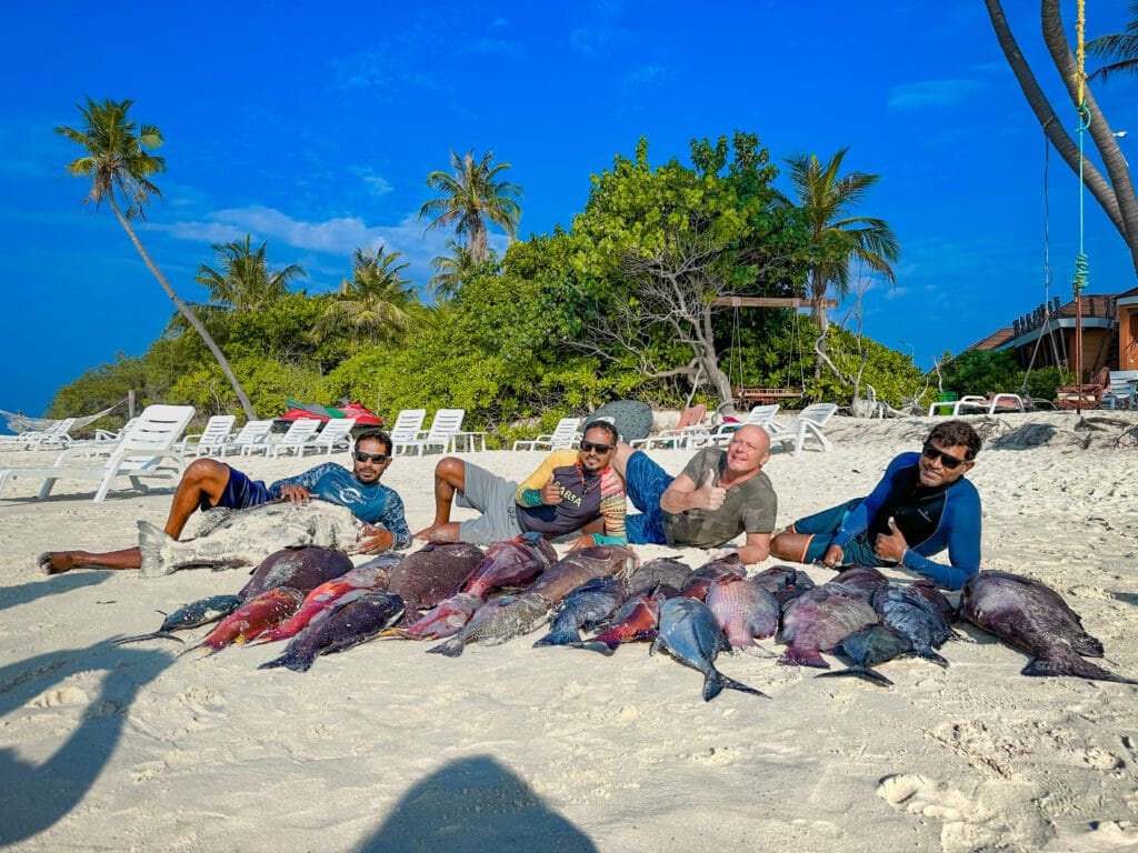 Guests proudly displaying their caught fish on the beach of Fodhdhoo Island, Maldives, during a budget-friendly fishing trip.