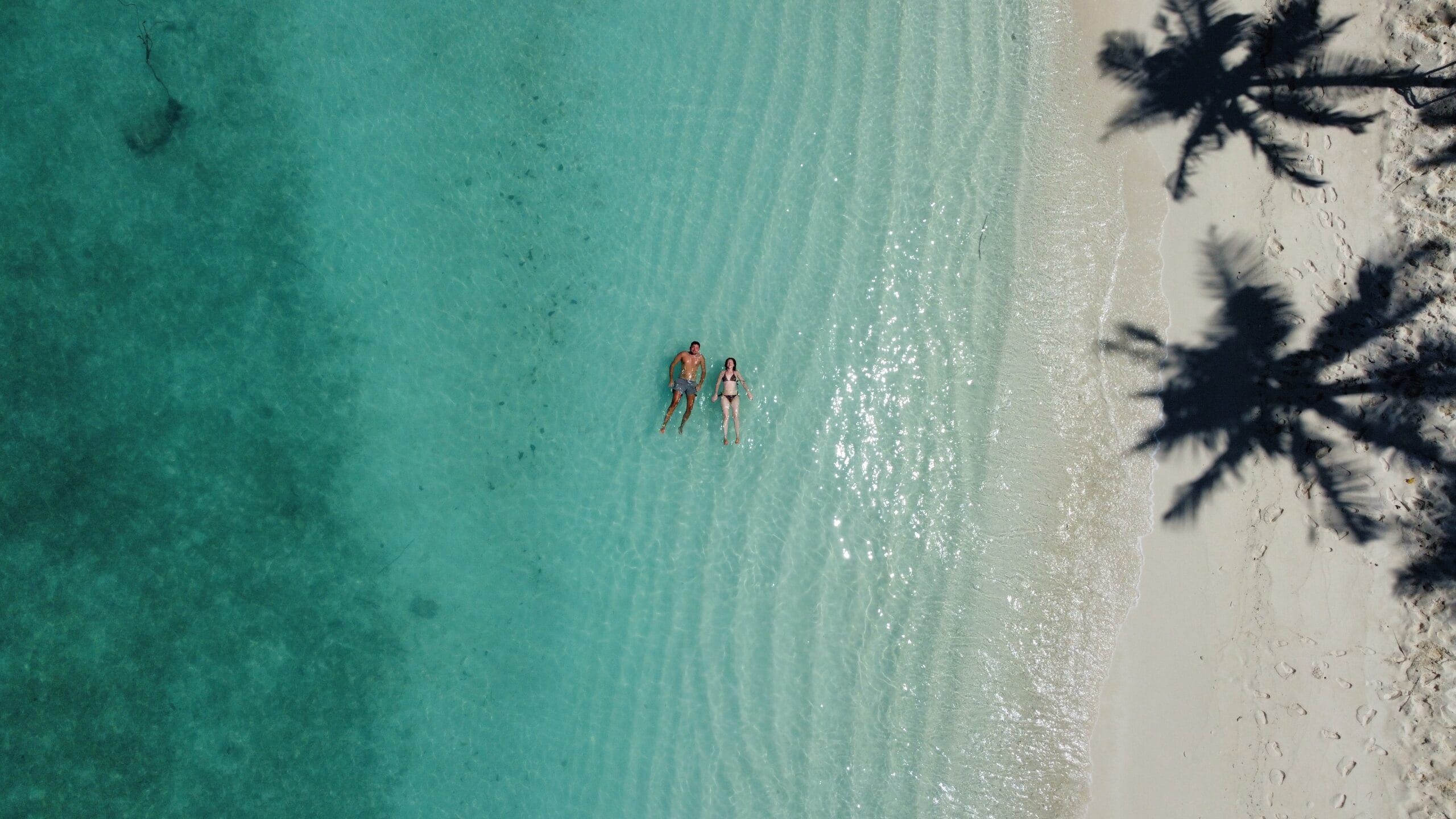 Smiling guests strolling hand-in-hand along gentle shoreline waves on Fodhdhoo