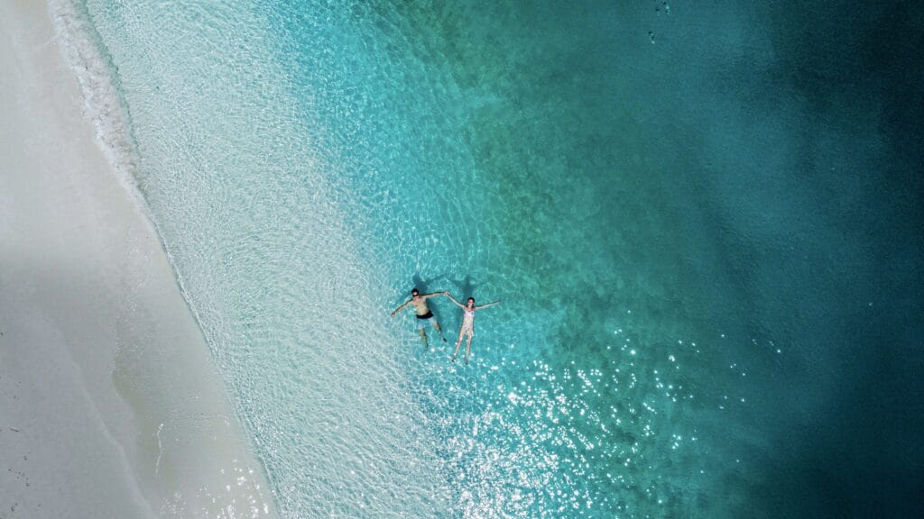 Aerial picture of a couple floating on the ocean near the sandbank beach, enjoying their journey to Discover Maldives.