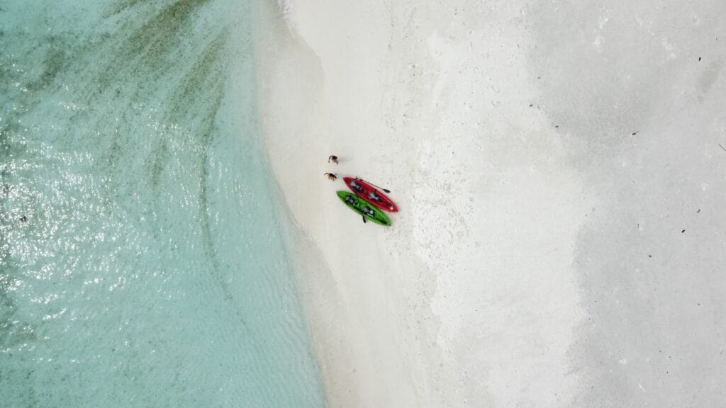 Aerial picture of a couple landing on a sandbank by canoe, enjoying an intimate retreat during their romantic getaway Maldives guesthouse stay.