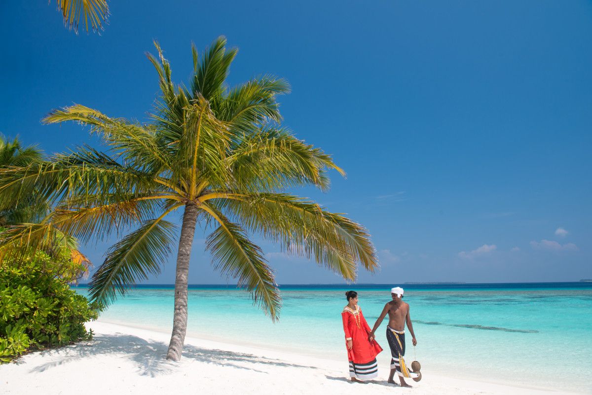 Couples strolling in local attire, celebrating culture amid Fodhdhoo’s tranquil shores