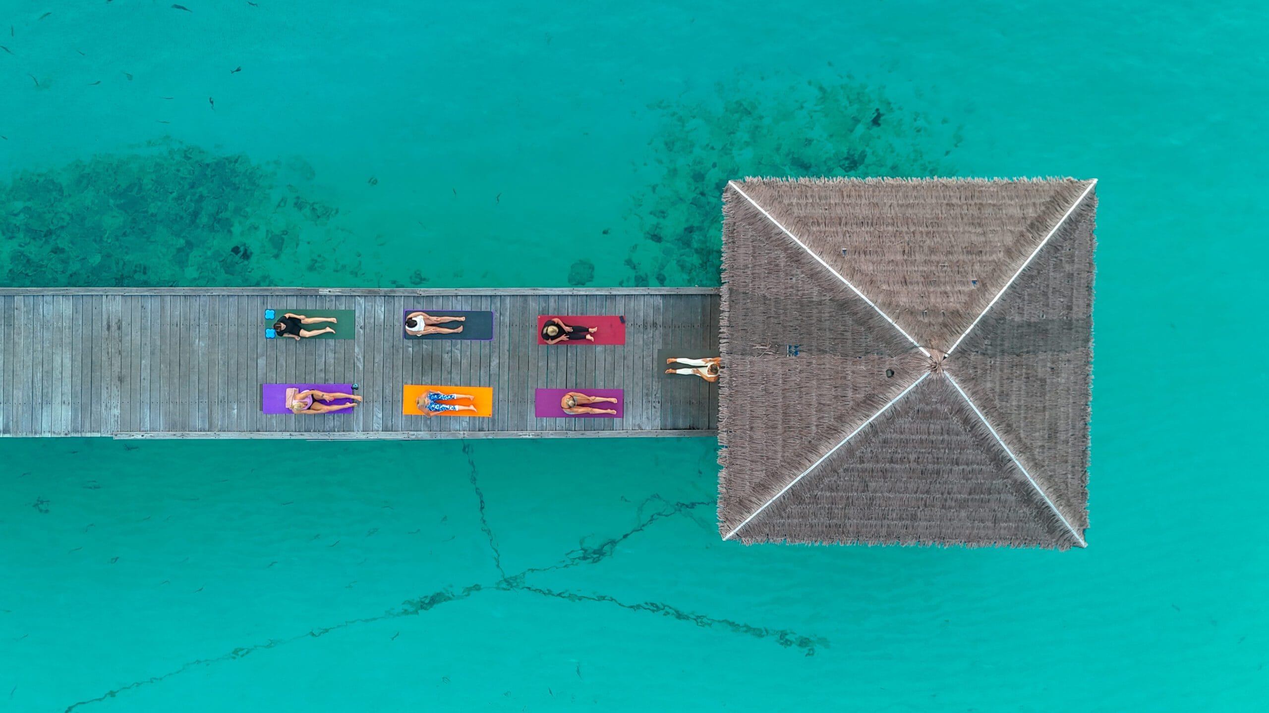 High-angle shot of guests practicing sunrise yoga on Fodhdhoo arrival jetty, part of mindful Holidays to the Maldives