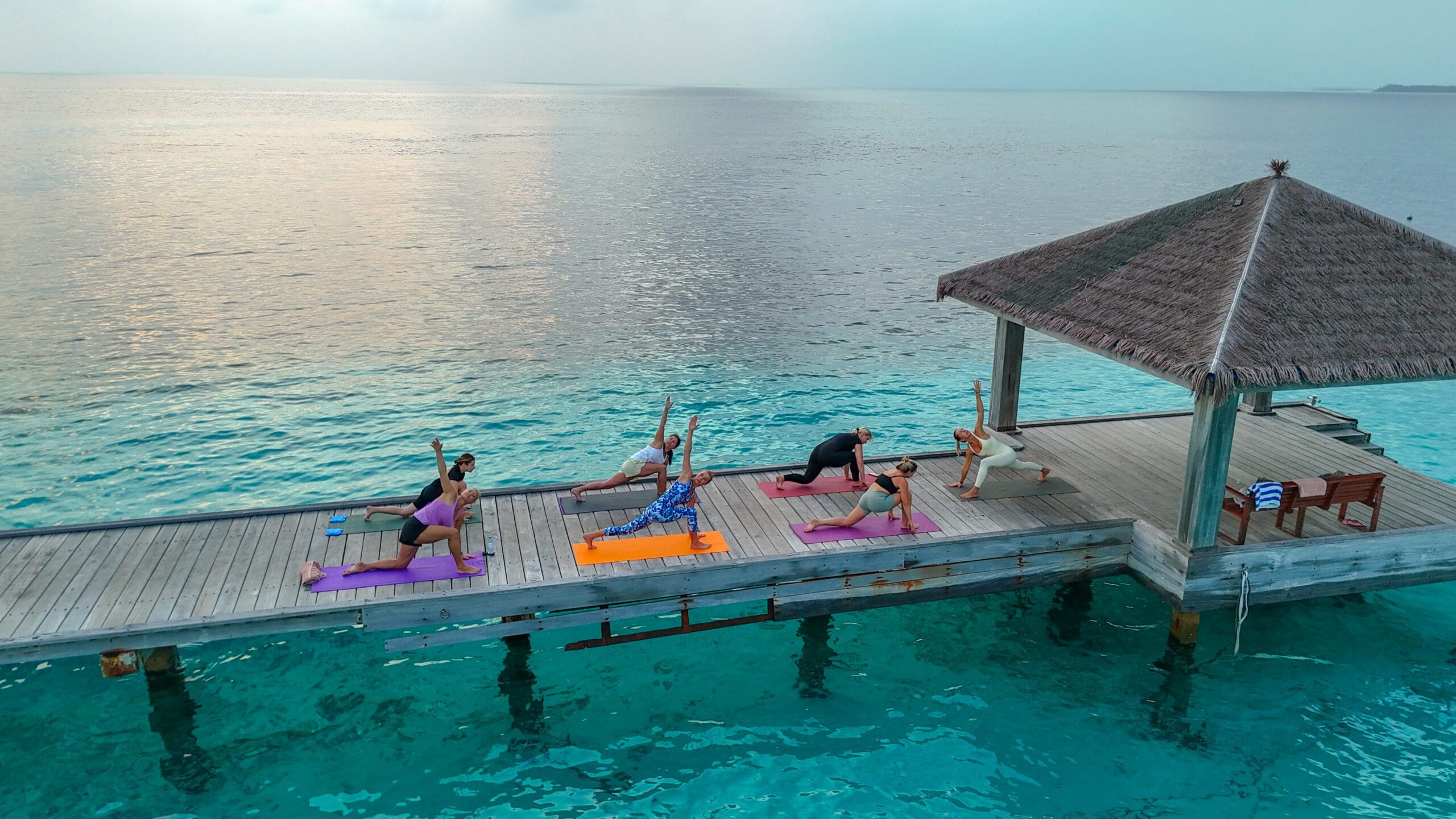 Visitors practicing sunrise yoga on the wooden arrival jetty as gentle waves roll below