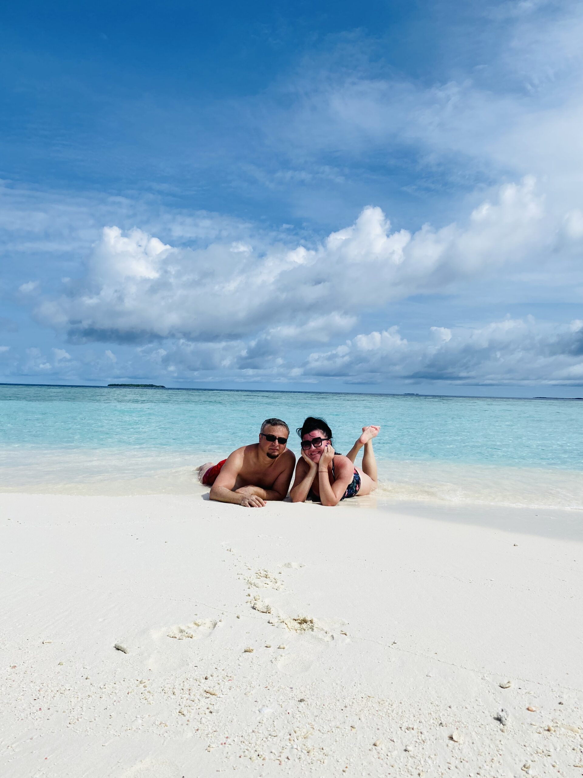 Relaxed duo resting on soft sand, treasuring a carefree Holiday To The Maldives memory
