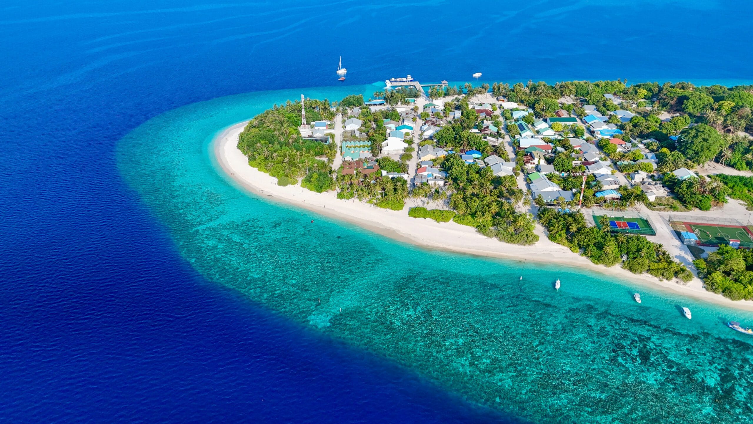 Drone view of distant Fodhdhoo Island framed by turquoise reef on an Adventurous Holiday at Maldives